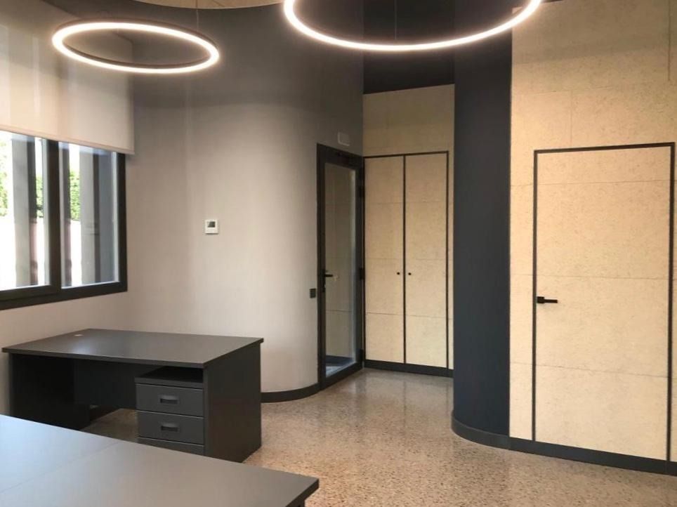 Interior de oficina moderno con escritorio negro, paredes grises, lámparas de techo circulares y dos puertas.