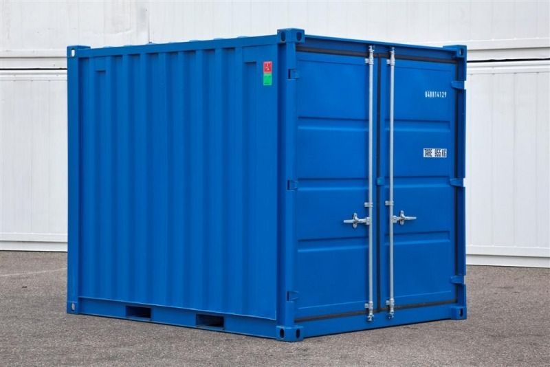 Contenedor de transporte azul con puertas dobles en un terreno pavimentado.
