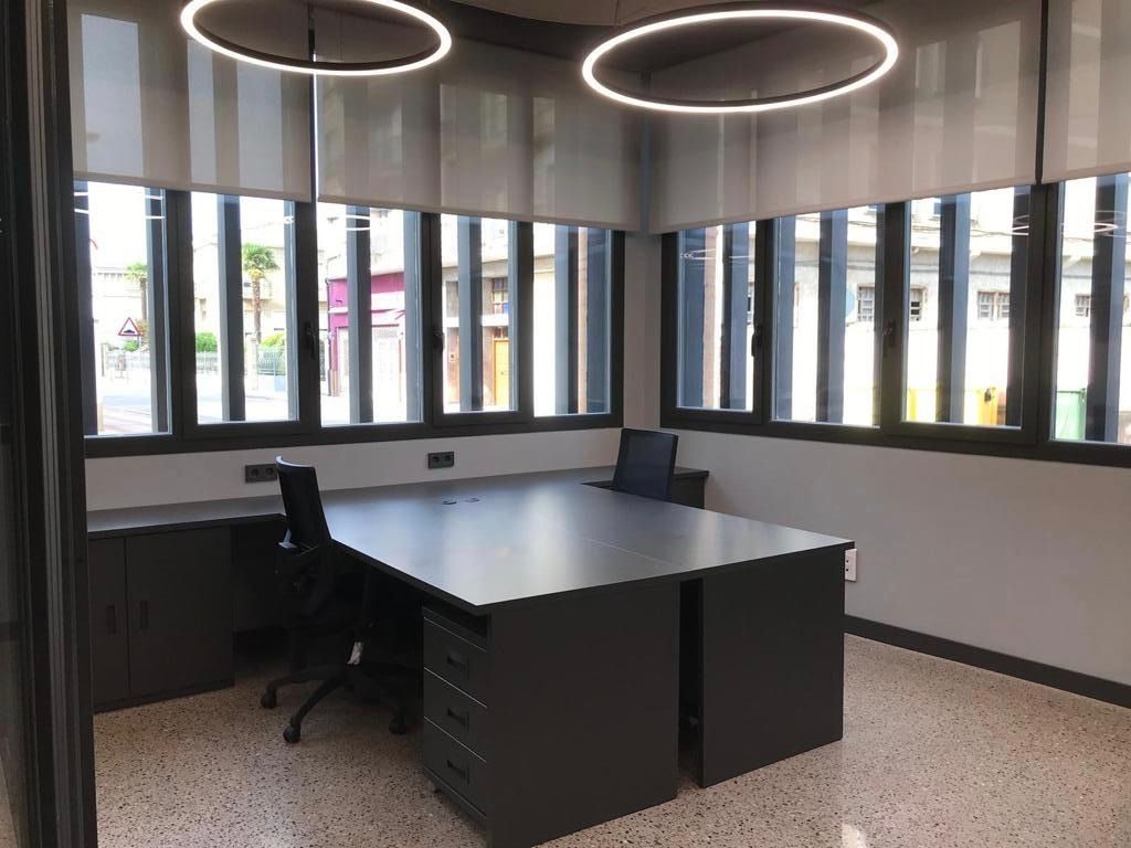 Sala de conferencias moderna con mesa oscura, sillas negras y grandes ventanales con iluminación circular en el techo.