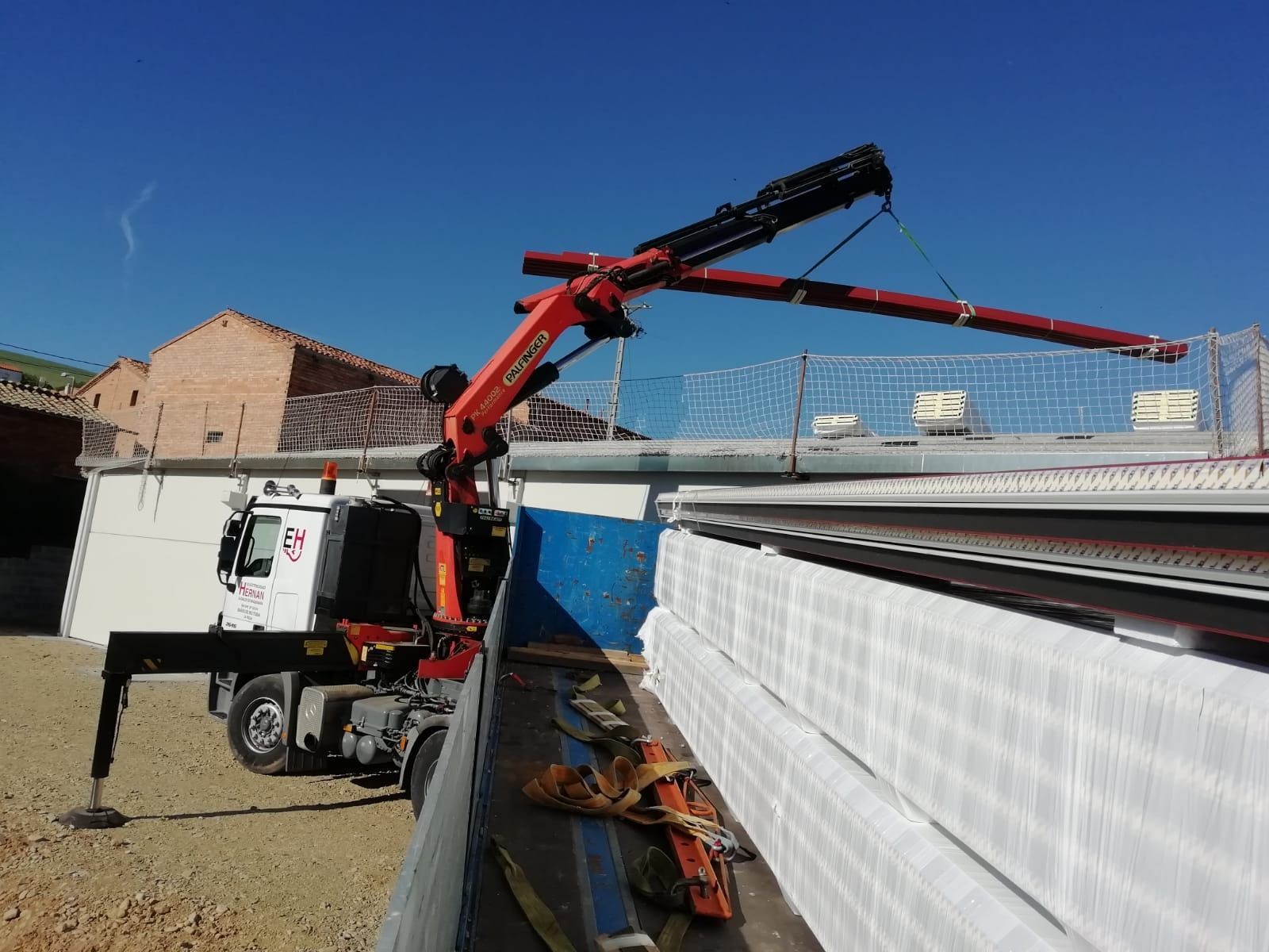 Un camión bomba de hormigón vertiendo hormigón en una obra de construcción junto a una pared blanca en un día soleado.