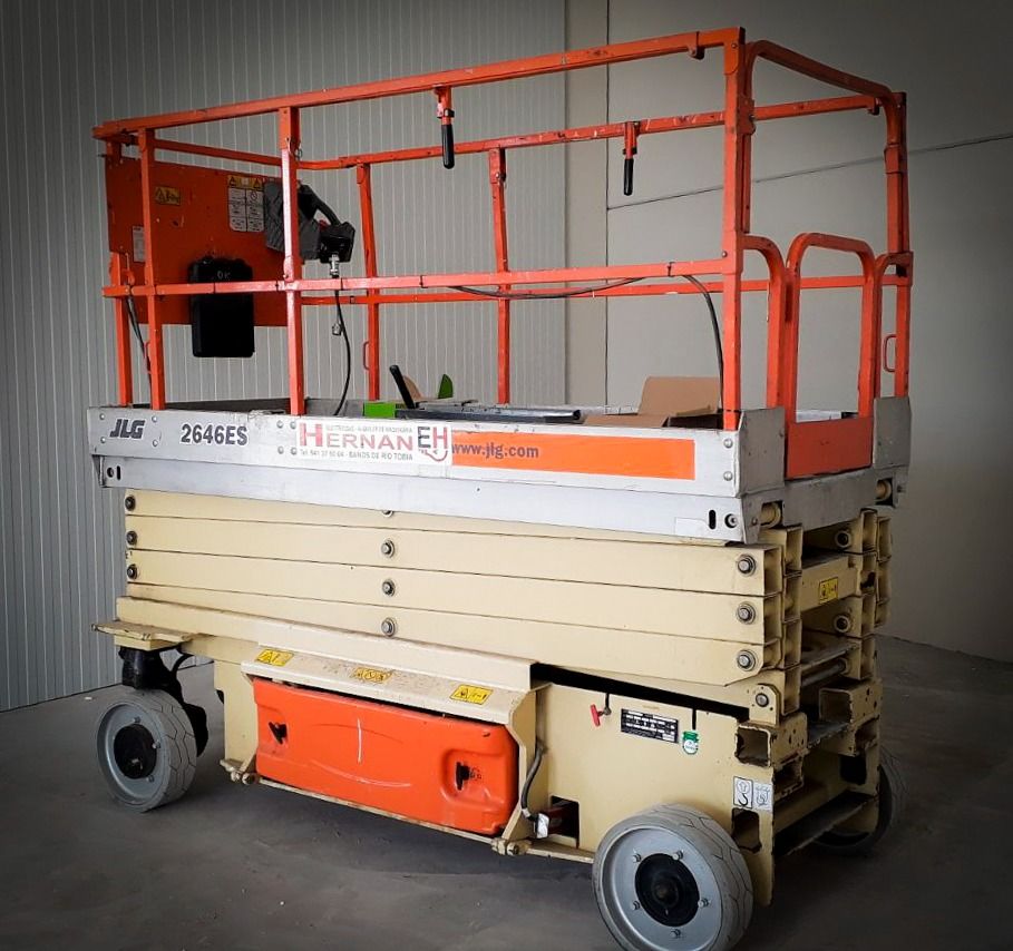 Plataforma elevadora de tijera naranja y beige con barandillas de seguridad, estacionada en el interior de un almacén.