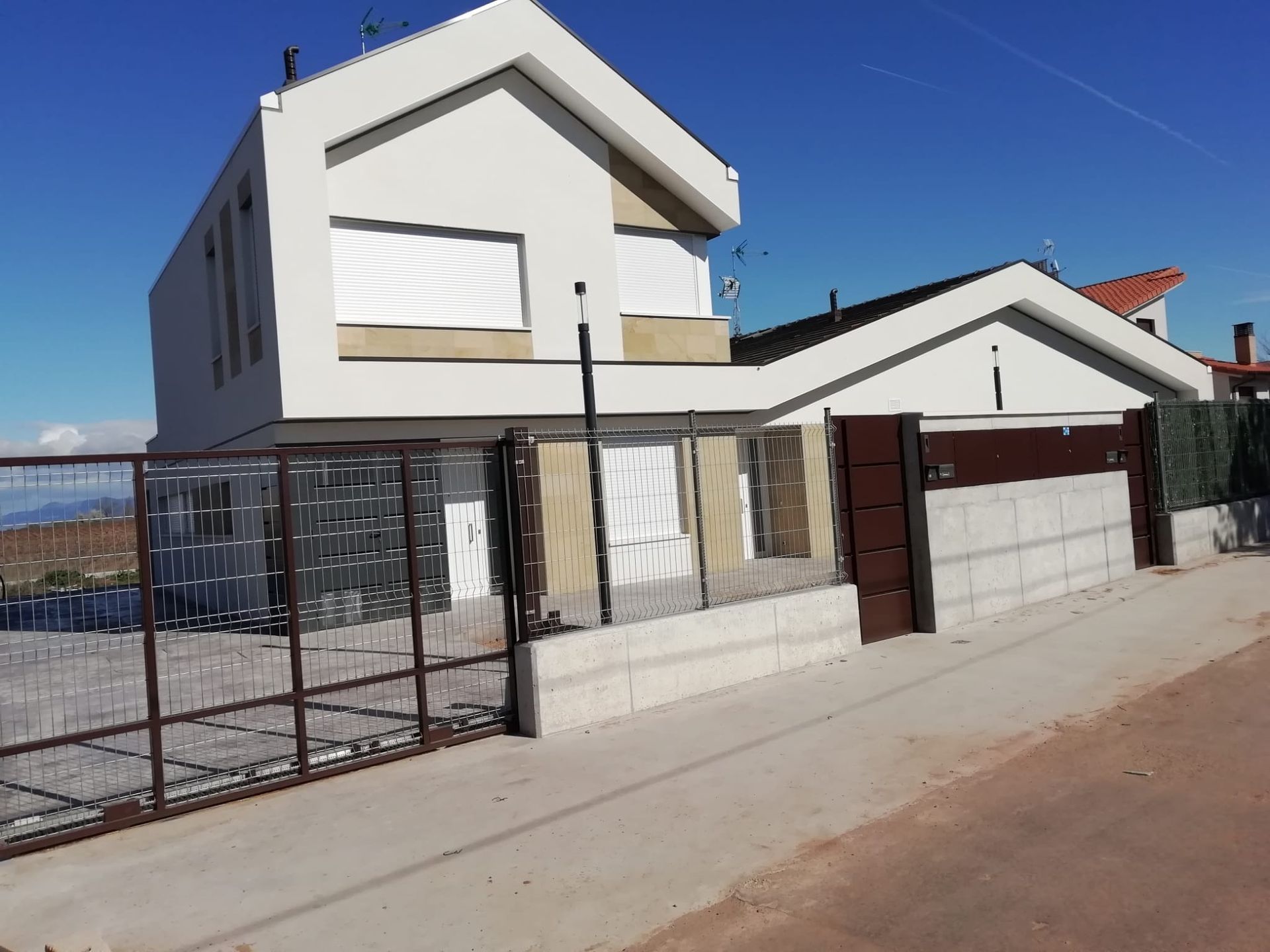 Casa moderna de dos plantas con paredes blancas, patio delantero cercado y entrada para vehículos en una calle residencial.