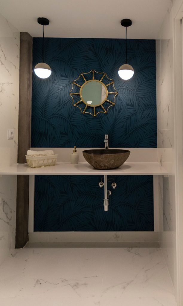 Tocador de baño moderno con pared decorativa azul, espejo redondo, lámparas colgantes y lavabo sobre encimera.