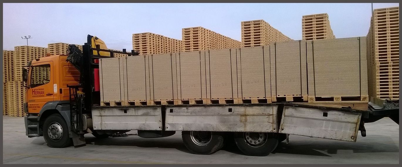 Camión naranja cargado con cajas de cartón apiladas y grandes paneles en una carretera.