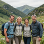 Cuatro excursionistas con mochilas de pie en un valle verde de montaña, sonriendo a la cámara