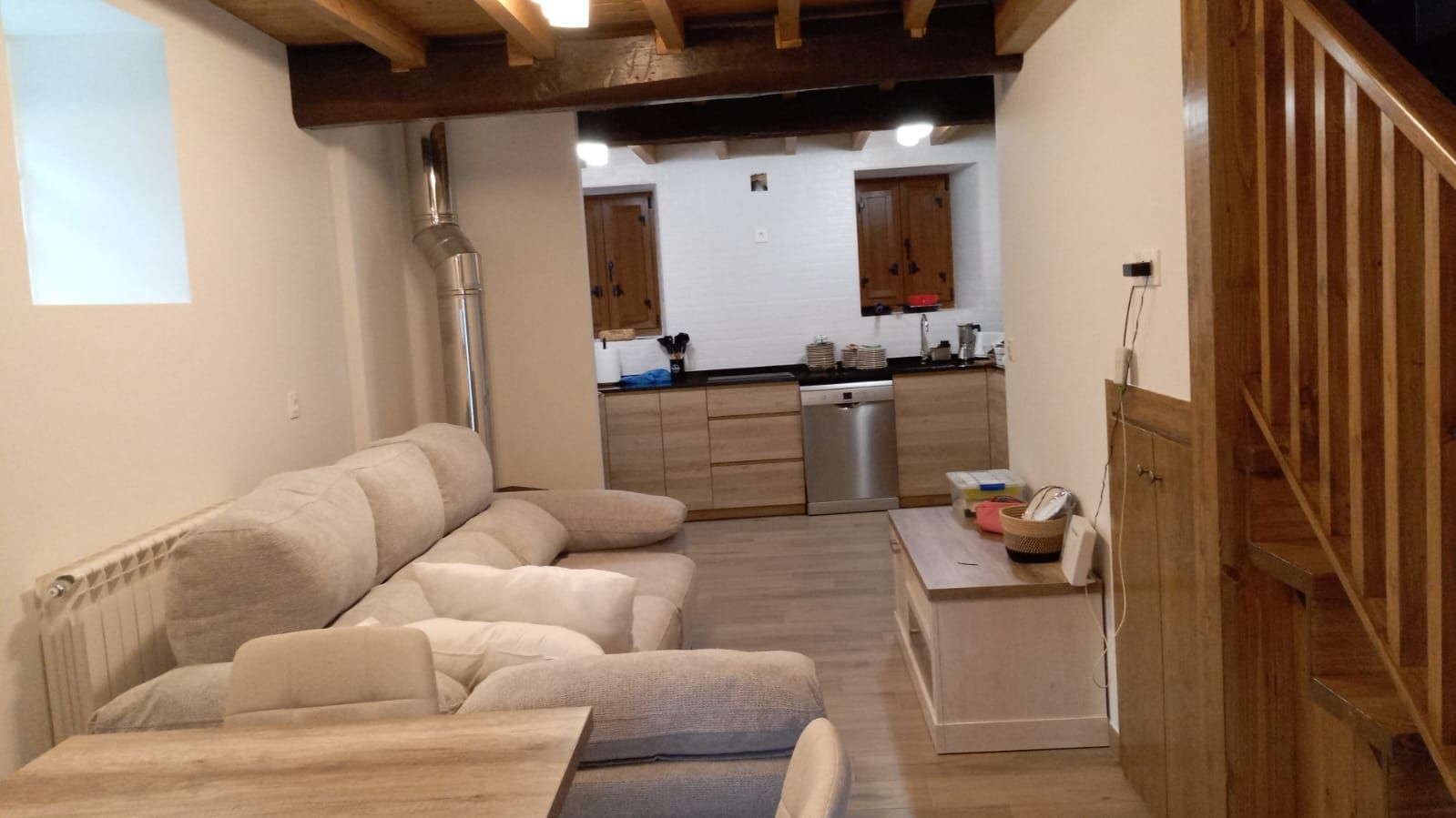 Salón rústico de piedra con techo de madera, sofás beige y grandes ventanales con vistas a un paisaje luminoso