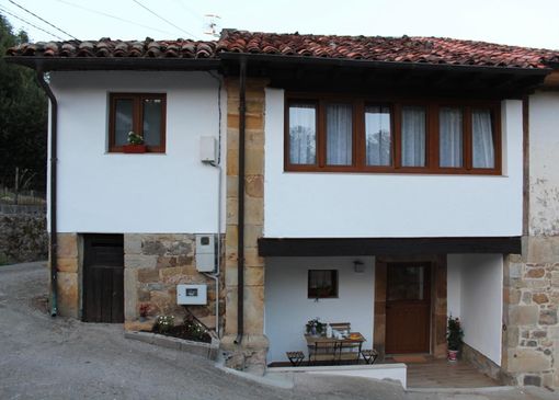 Casa de piedra con tejado de pizarra en un prado verde de montaña bajo un cielo nublado