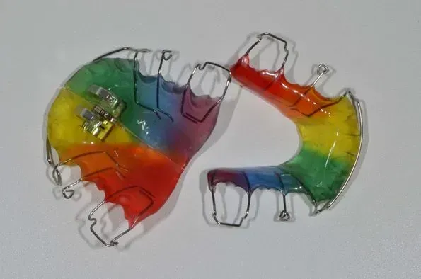 Ein Paar regenbogenfarbene Zahnspangen auf einer weißen Oberfläche, Dentaltechnik Claudia Meier
