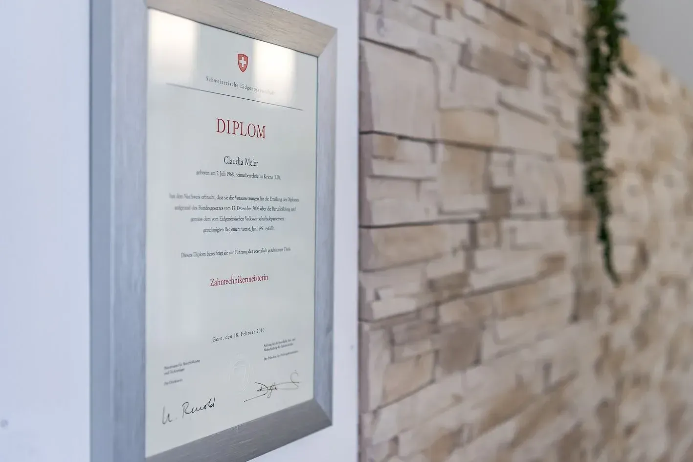 Ein gerahmtes Zertifikat hängt an einer Ziegelwand, Dentaltechnik Claudia Meier