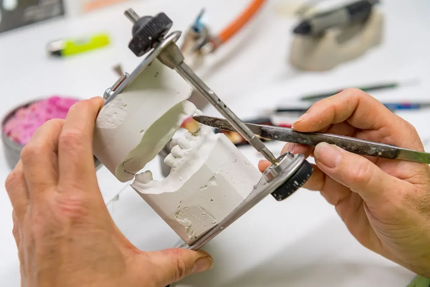 Eine Person bearbeitet mit einem Pinsel ein Zahnmodell. Dentaltechnik Claudia Meier