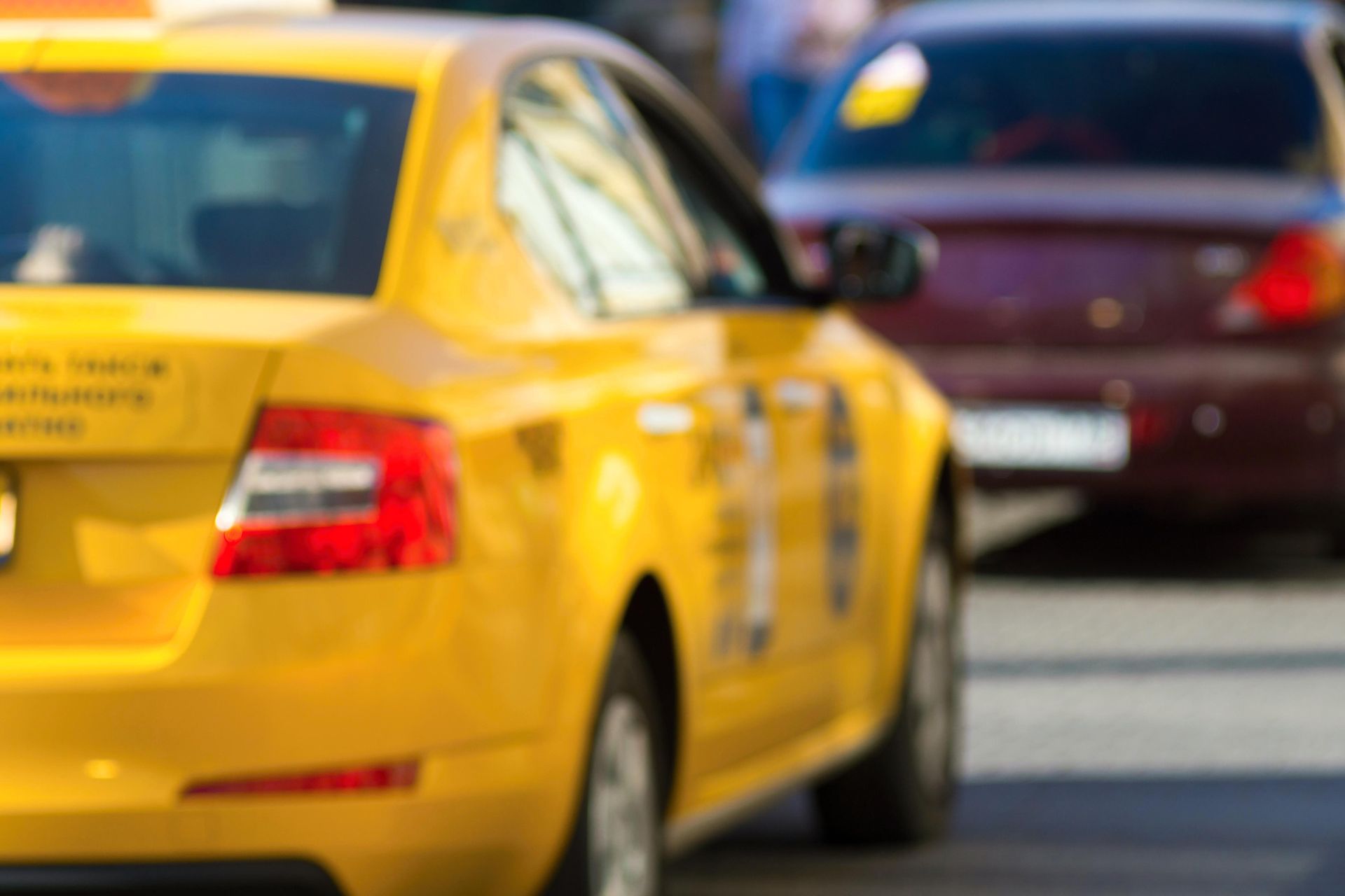 Un taxi amarillo en una calle de la ciudad, con un coche rojo al fondo, ambos ligeramente borrosos.