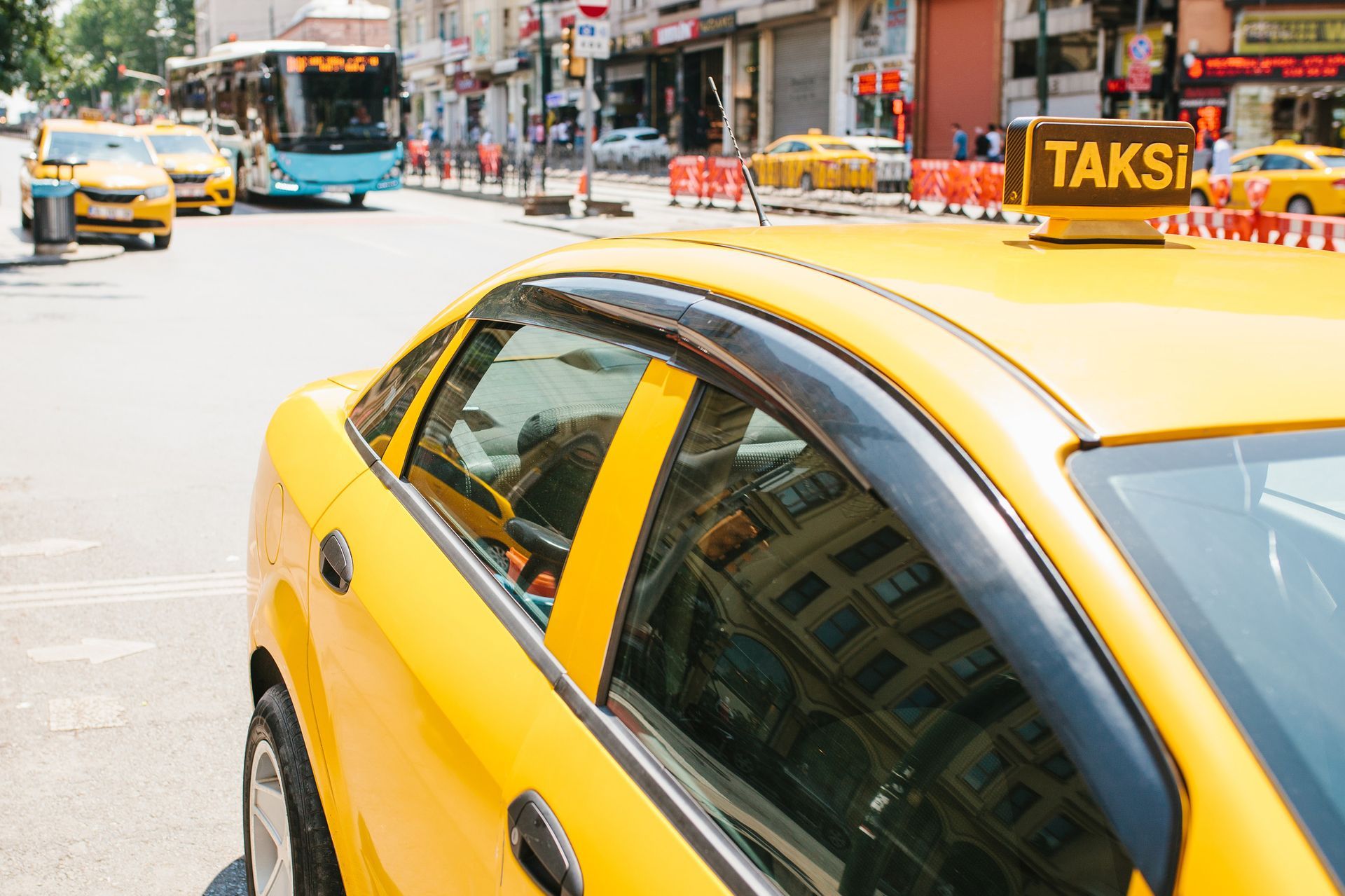 Taxi amarillo en una calle de la ciudad, otros taxis y un autobús al fondo.