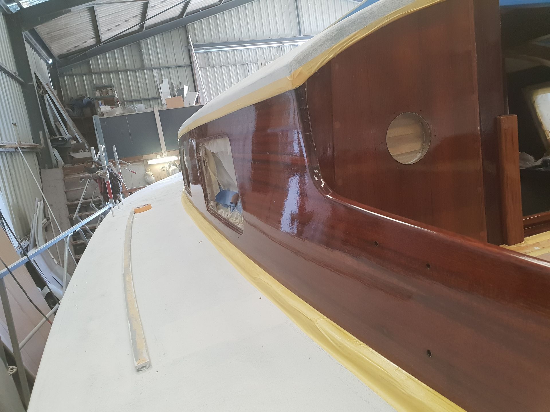 Gros plan sur le côté en bois verni de la cabine d'un bateau, masqué avec du ruban adhésif, à côté d'un pont blanc fraîchement peint.