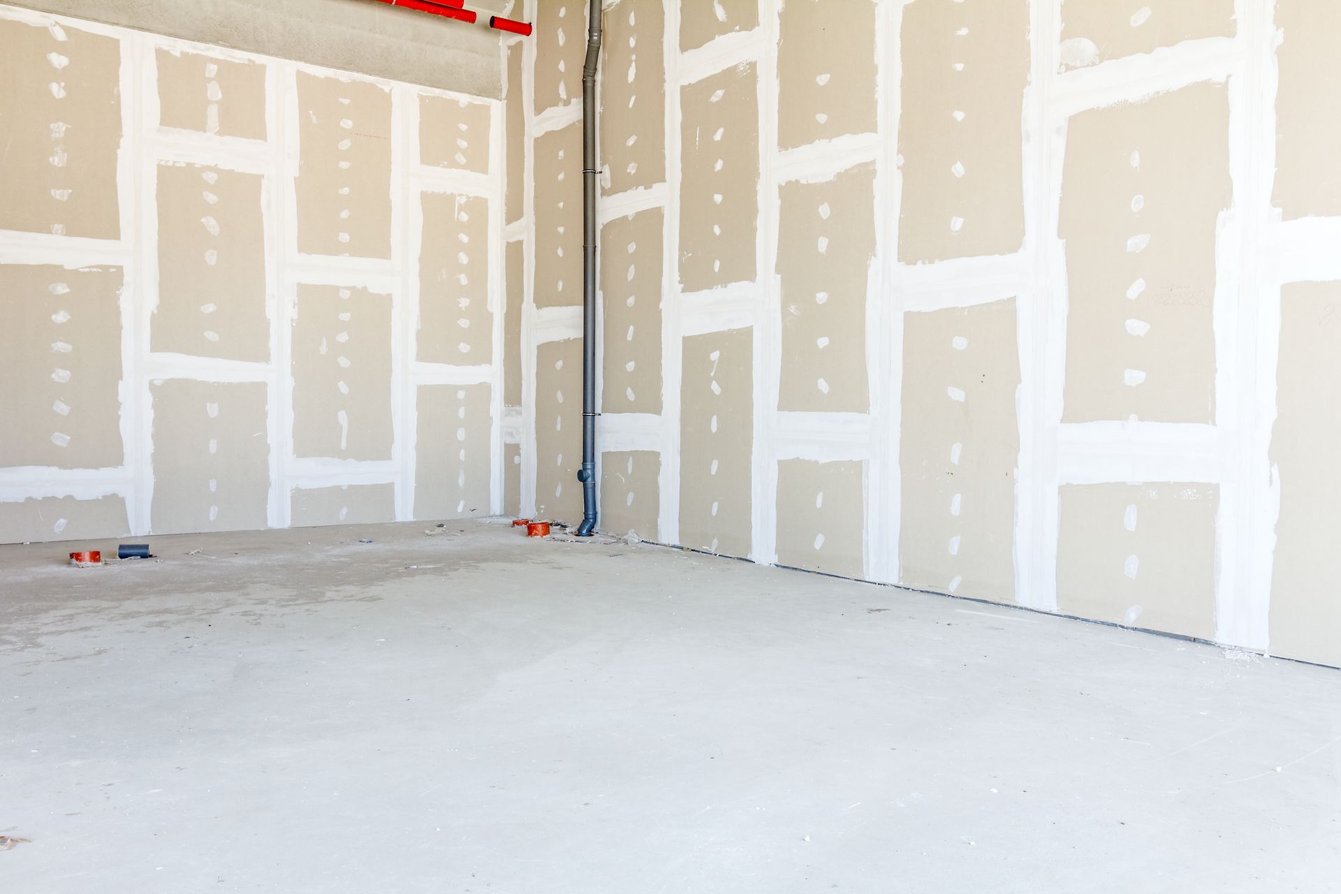 Pièce intérieure inachevée avec des panneaux de plaques de plâtre assemblés par un enduit blanc et un sol en béton.
