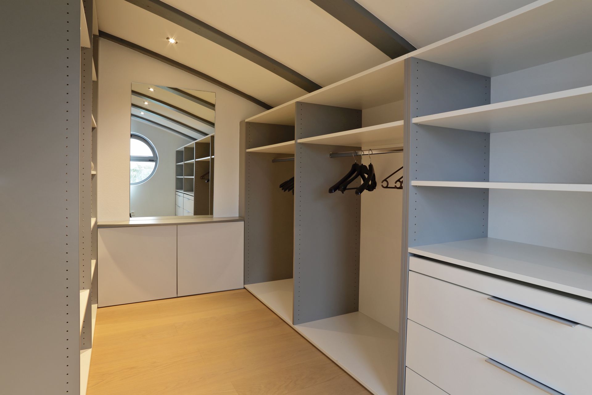 Dressing moderne avec étagères grises, tringles à vêtements, tiroirs blancs et miroir de courtoisie intégré.