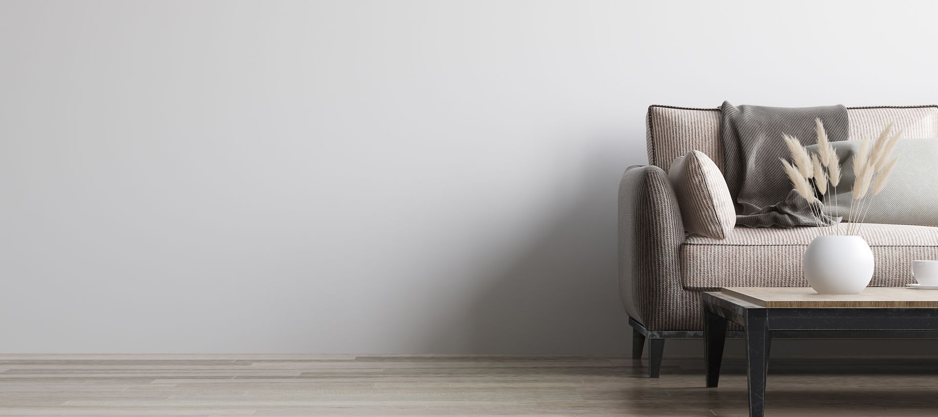 Un canapé beige à motifs, agrémenté d'un plaid, et une table basse avec un vase de fleurs séchées sont adossés à un mur blanc.