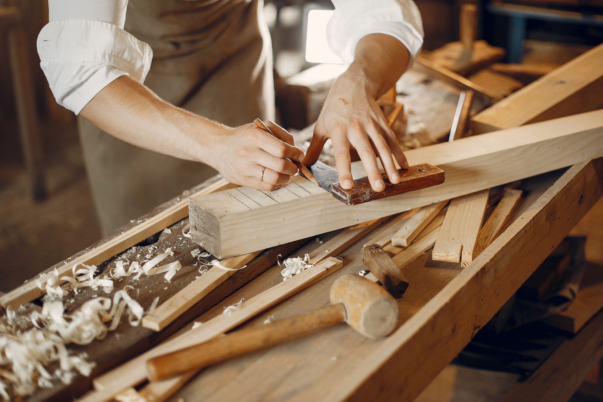 Un menuisier utilise un crayon et une équerre métallique pour marquer des mesures sur une pièce de bois dans son atelier.