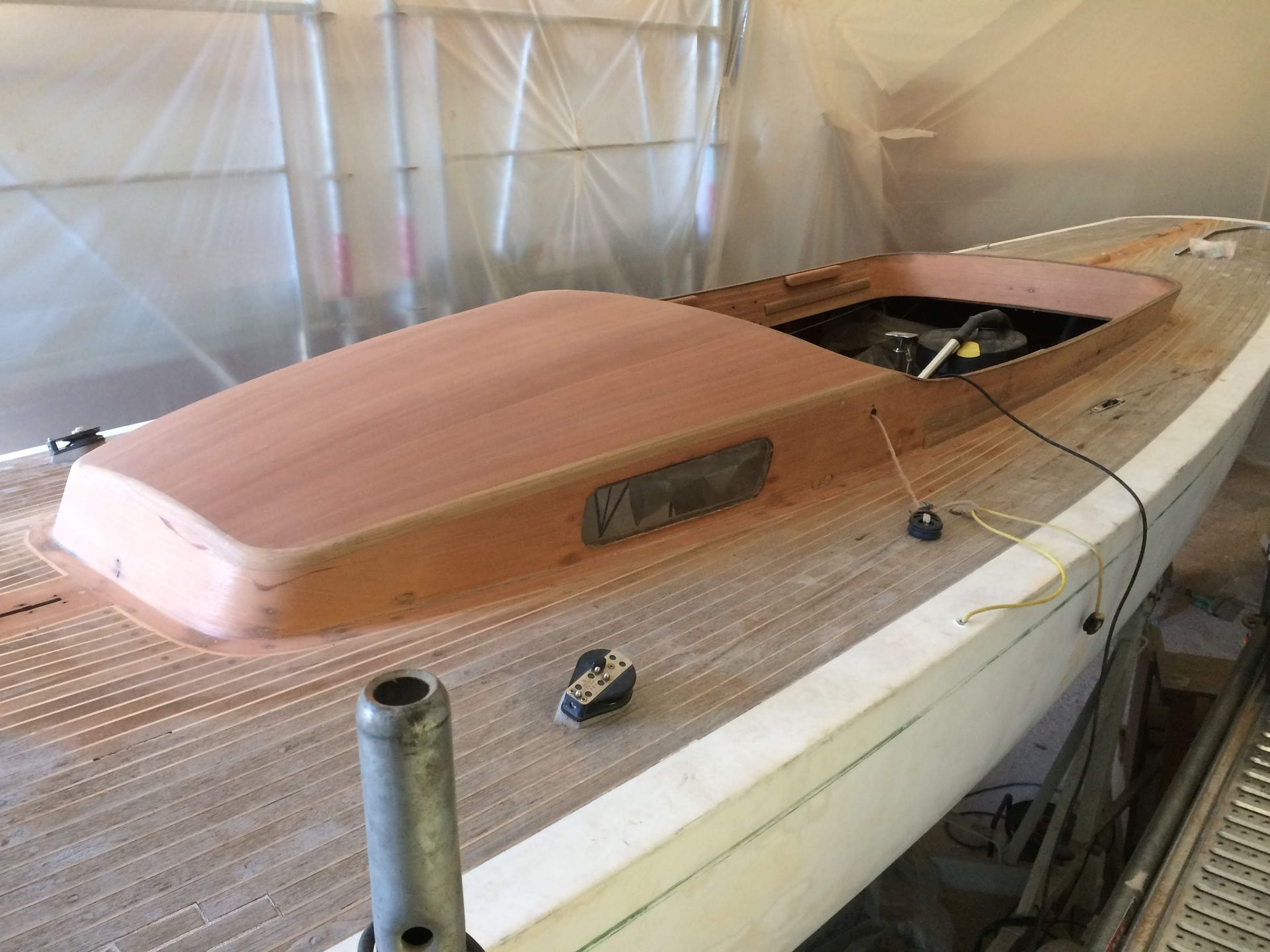 Une structure de cabine de bateau en bois repose sur un pont, avec des panneaux à grain de bois et un cockpit s'ouvrant sur un atelier.