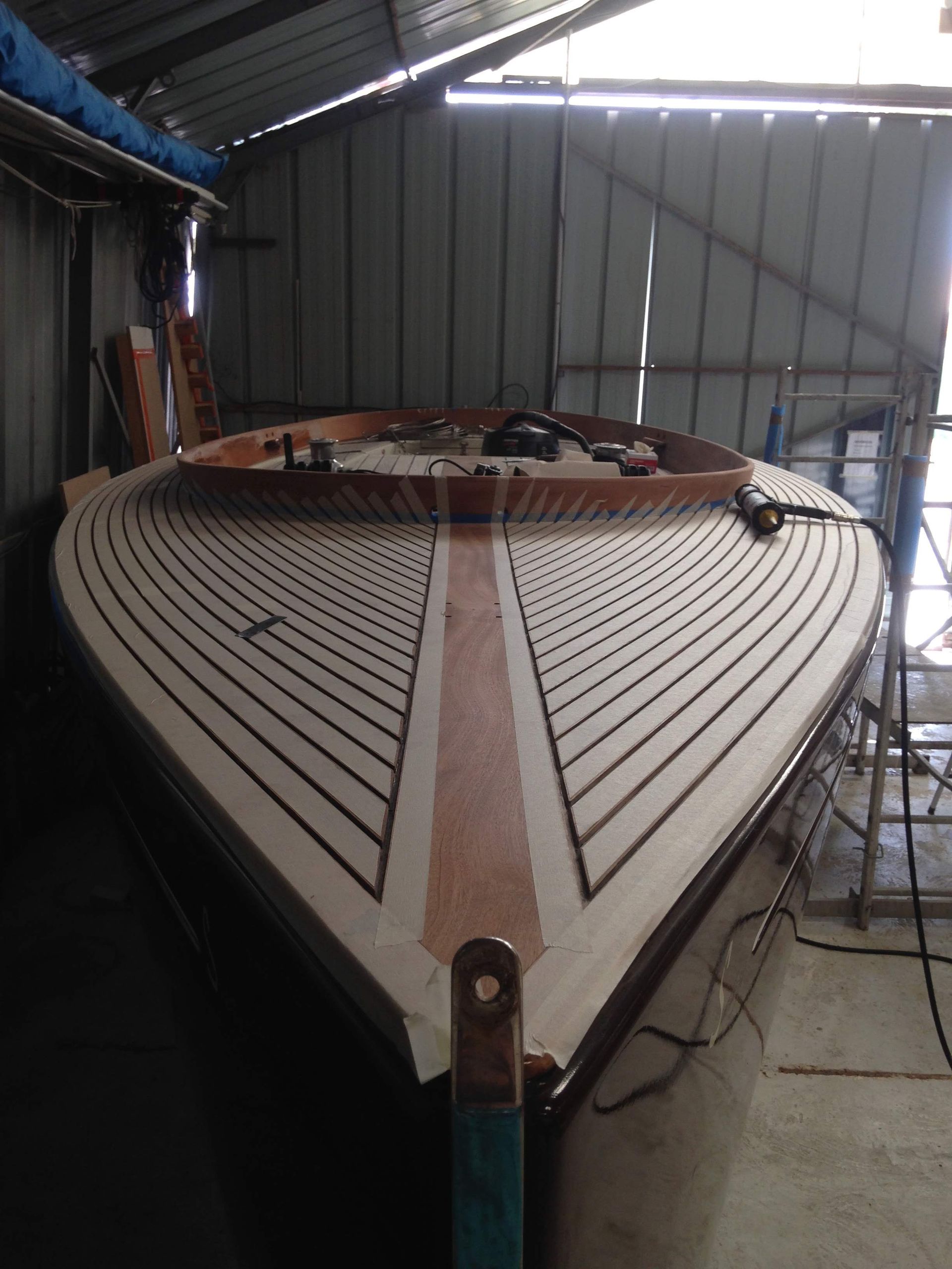 Le pont d'un bateau en bois en construction, composé de planches claires aux joints foncés, à l'intérieur d'un hangar.