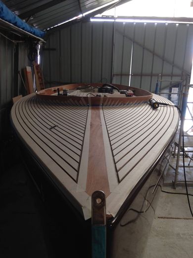 Dans un atelier, le pont d'un bateau en construction, avec ses planches de bois clair, ses joints de calfeutrage foncés et sa bande centrale.