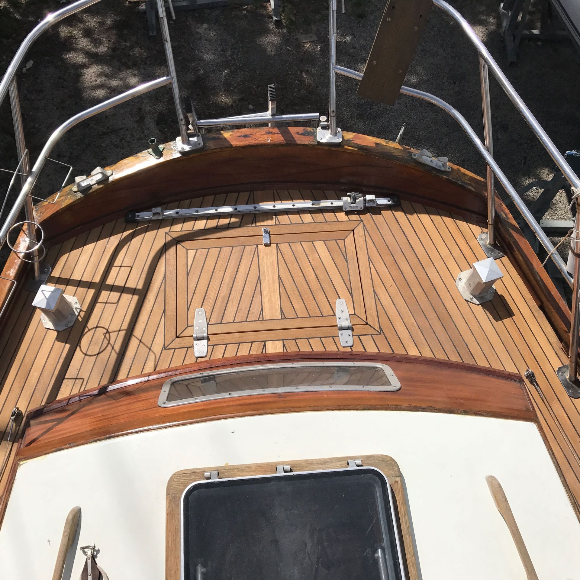 Vue aérienne du pont en bois d'un bateau, comportant une trappe, des rambardes métalliques et des accessoires.