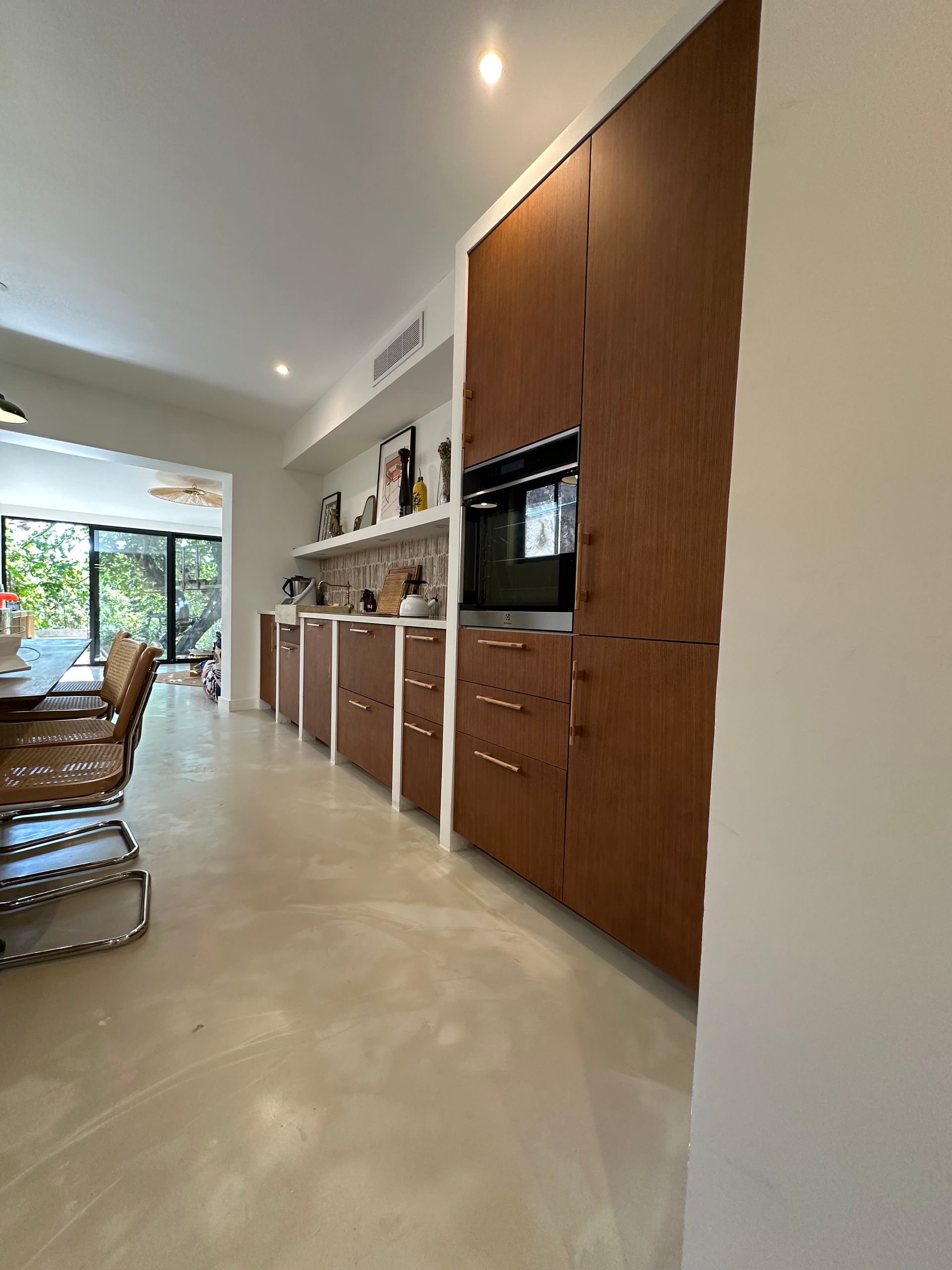 Une cuisine moderne avec de hauts placards en bois foncé, un four encastré et un sol clair et élégant.