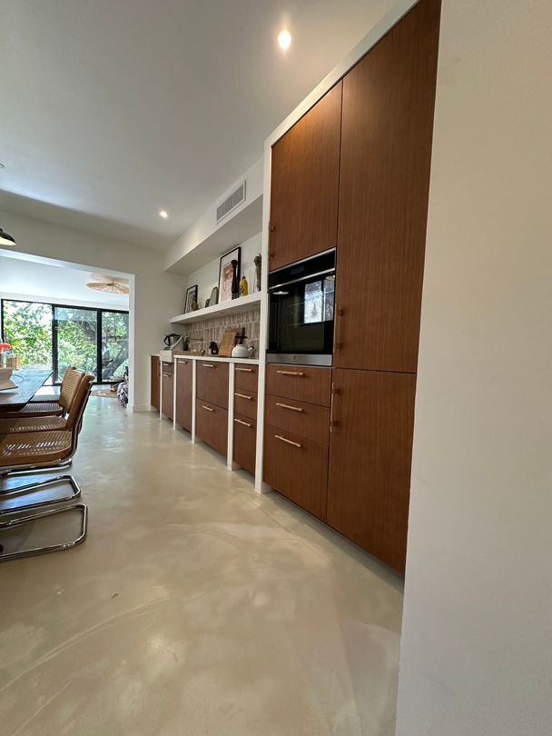 Une cuisine moderne dotée de hauts placards en bois foncé, d'un four encastré et d'un long comptoir, le tout dans un espace ouvert et lumineux.