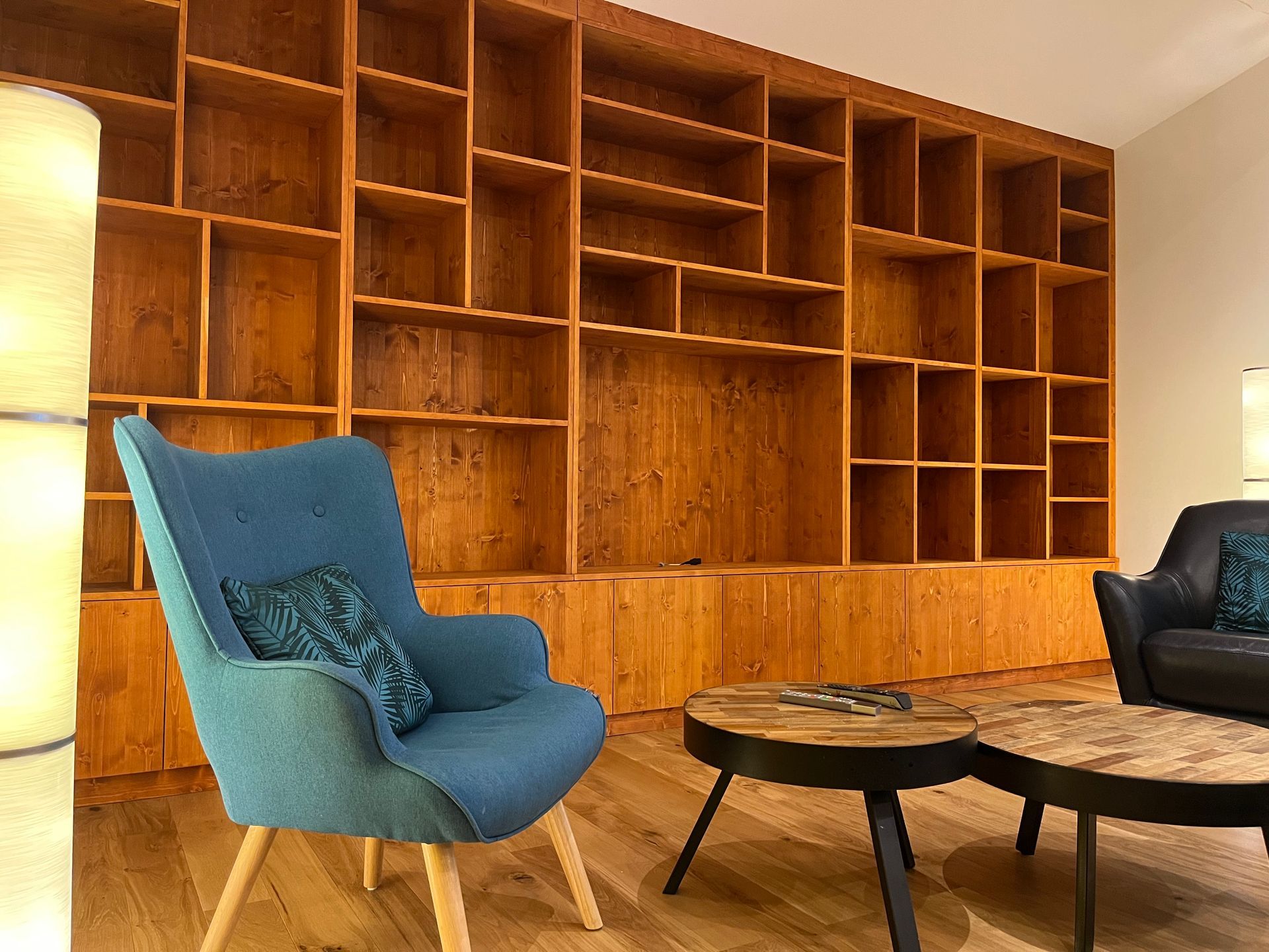 Un fauteuil turquoise et des tables basses rondes sont disposés devant une grande bibliothèque en bois sur mesure, allant du sol au plafond.