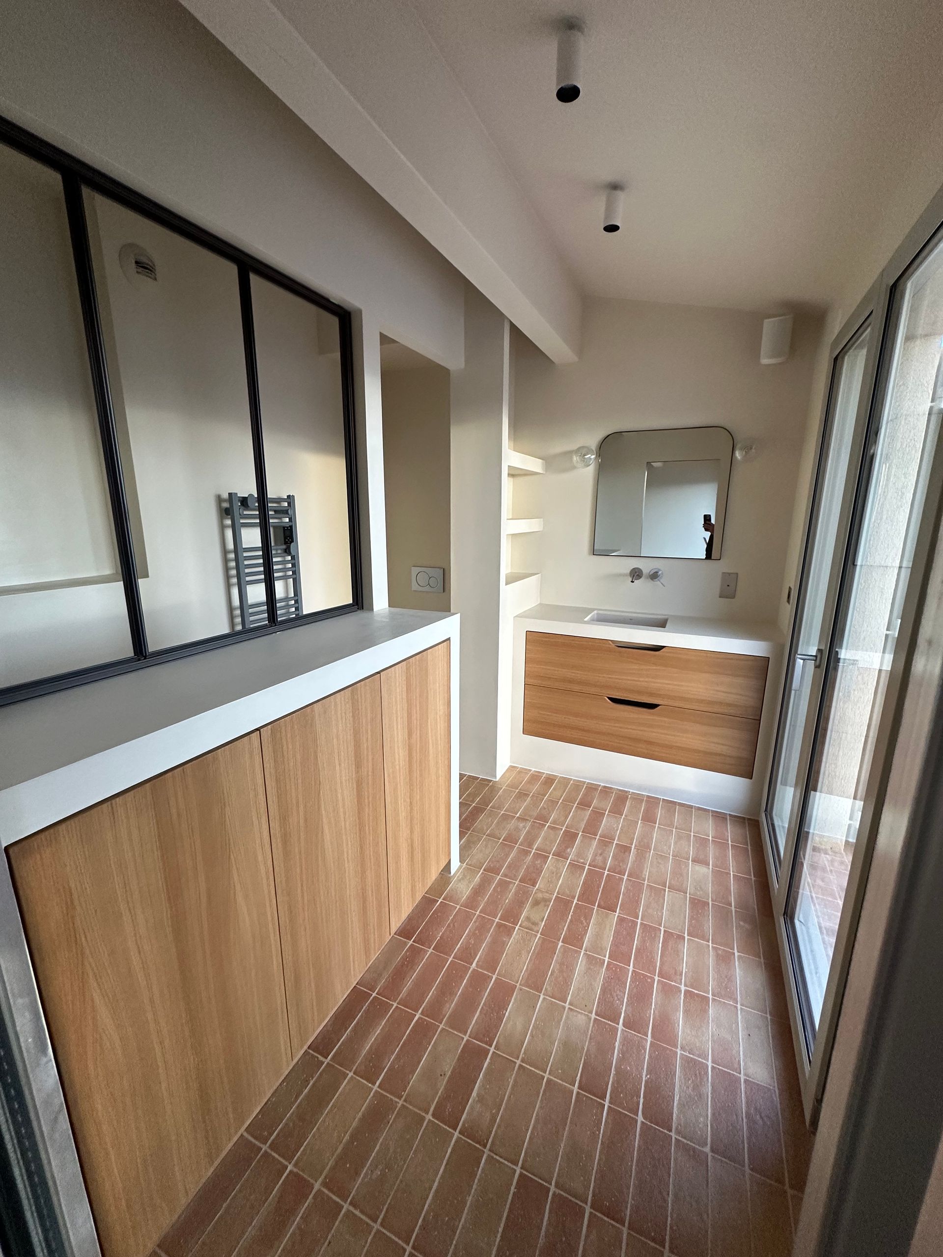 Intérieur de salle de bains moderne avec meubles en bois, miroir au-dessus d'un meuble-lavabo et sol carrelé style terre cuite.