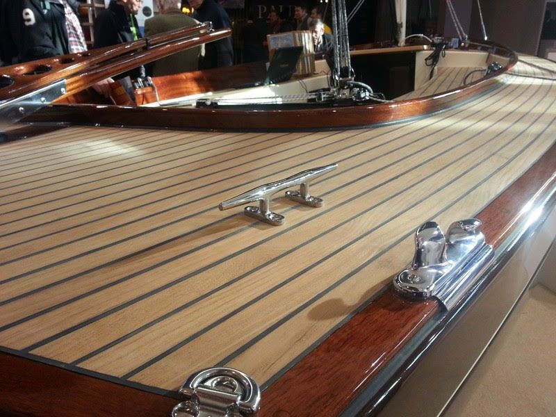 Gros plan sur le pont en bois poli d'un bateau, avec taquets et garnitures chromés, dans un environnement d'exposition.