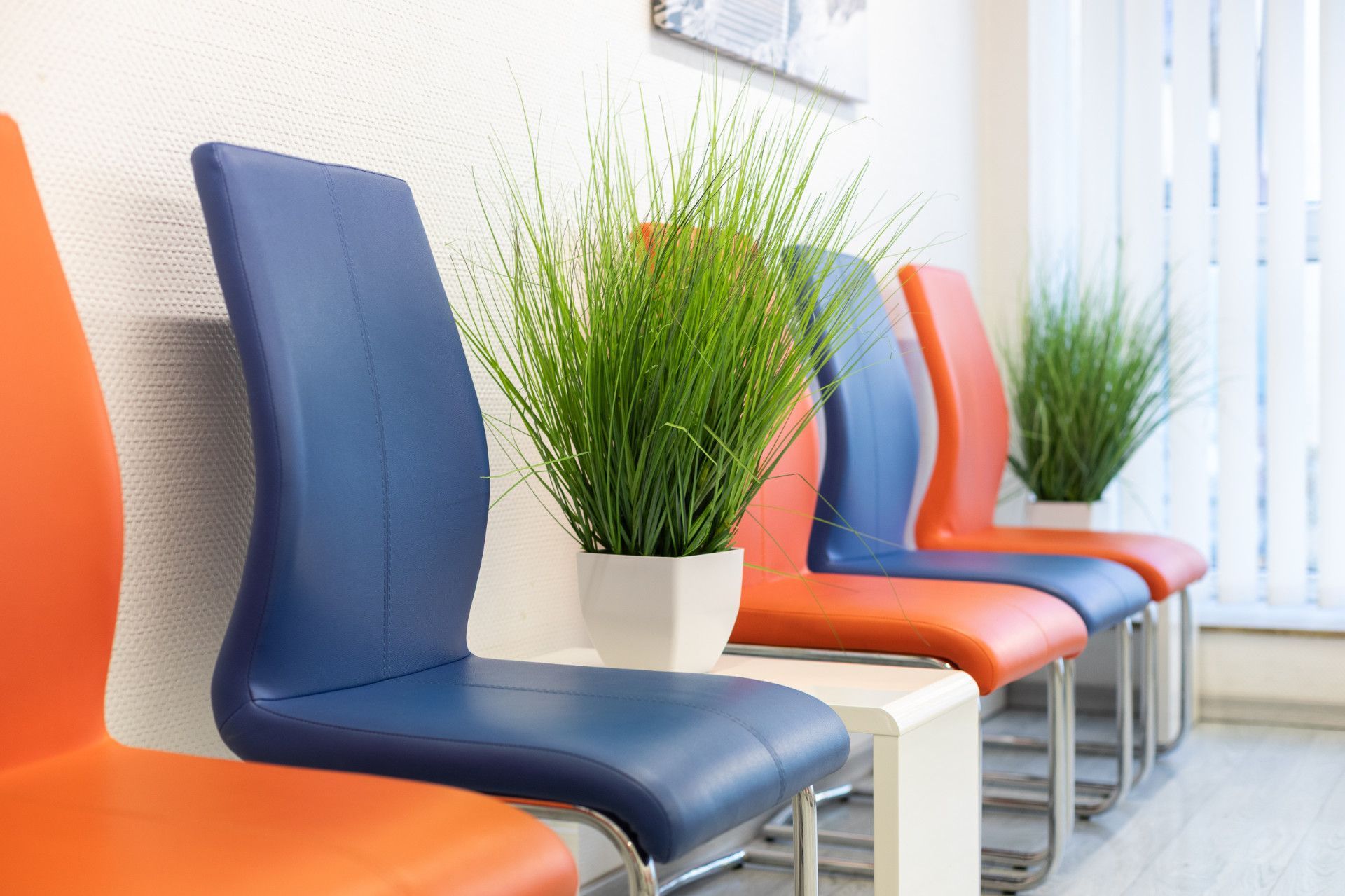 Eine Reihe bunter Stühle in einem Wartezimmer mit Topfpflanzen.