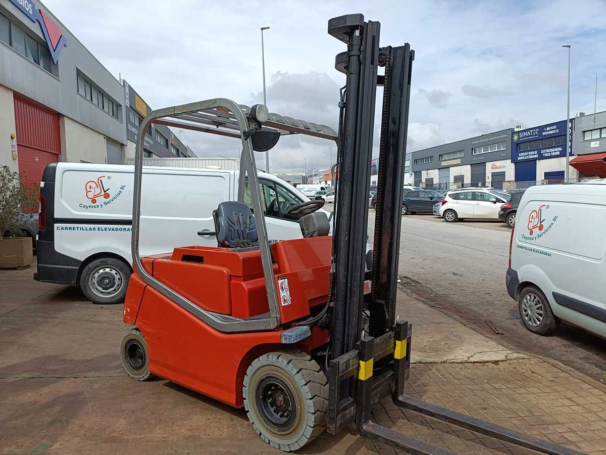 Una carretilla elevadora roja estacionada en un terreno industrial junto a furgonetas blancas y edificios de almacén.