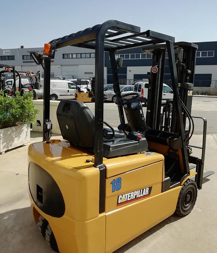 Una carretilla elevadora Caterpillar amarilla está estacionada al aire libre en un patio industrial.