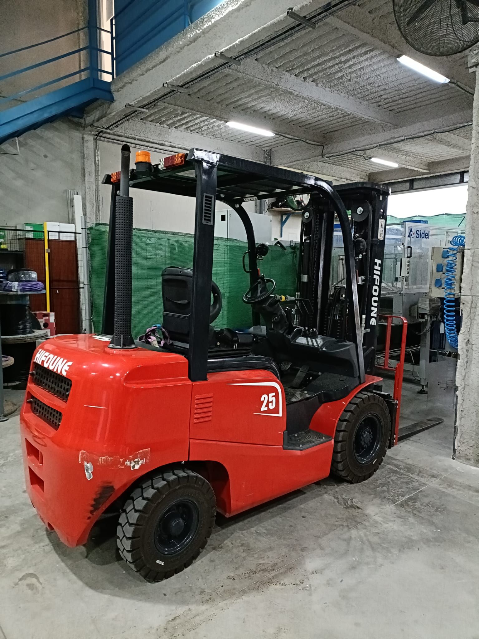 Una carretilla elevadora roja, con mástil negro y carrocería naranja, está aparcada en el interior de un almacén.