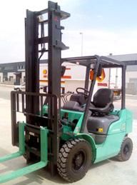 Una carretilla elevadora verde está estacionada al costado de la carretera frente a un edificio.