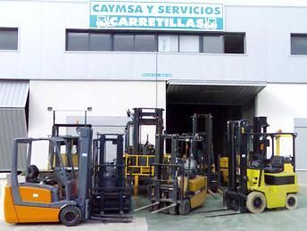 Varias carretillas elevadoras están estacionadas frente a un edificio que dice caymsa y servicios