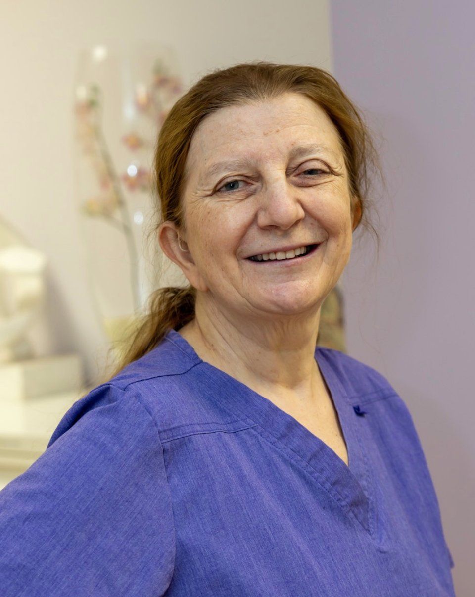 Frau mit langen, leuchtend roten Haaren lächelt in einem rosa Hemd in einem Büro.