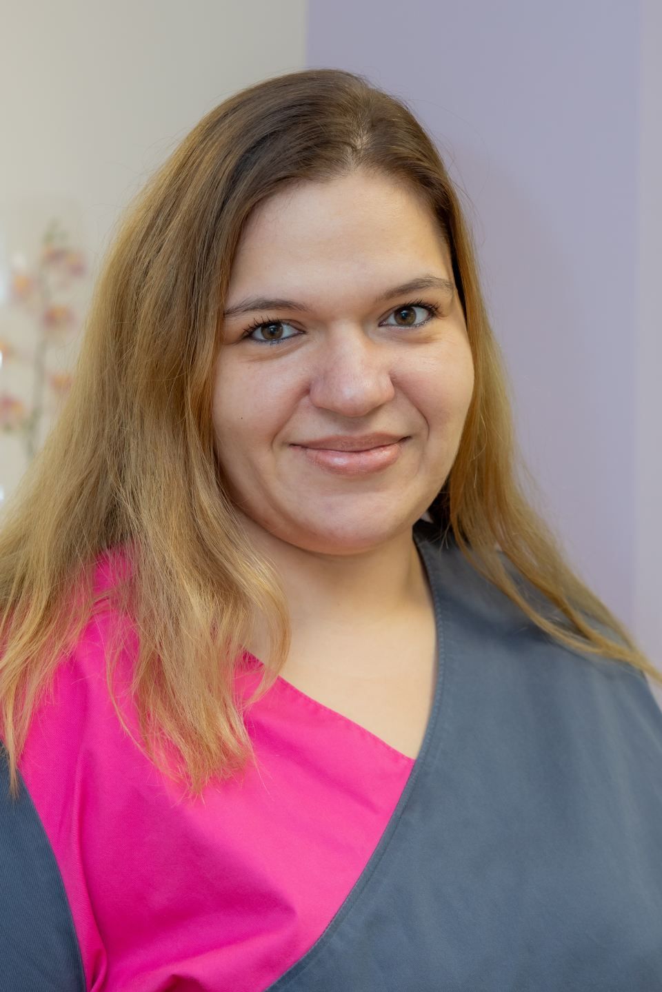 Frau mit langen, leuchtend roten Haaren lächelt in einem rosa Hemd in einem Büro.