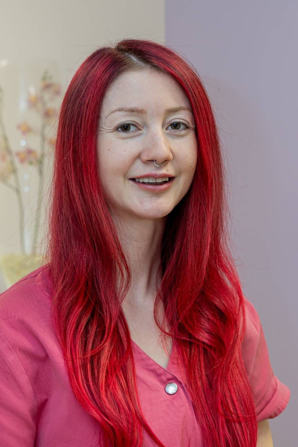 Frau mit langen, leuchtend roten Haaren lächelt in einem rosa Hemd in einem Büro.