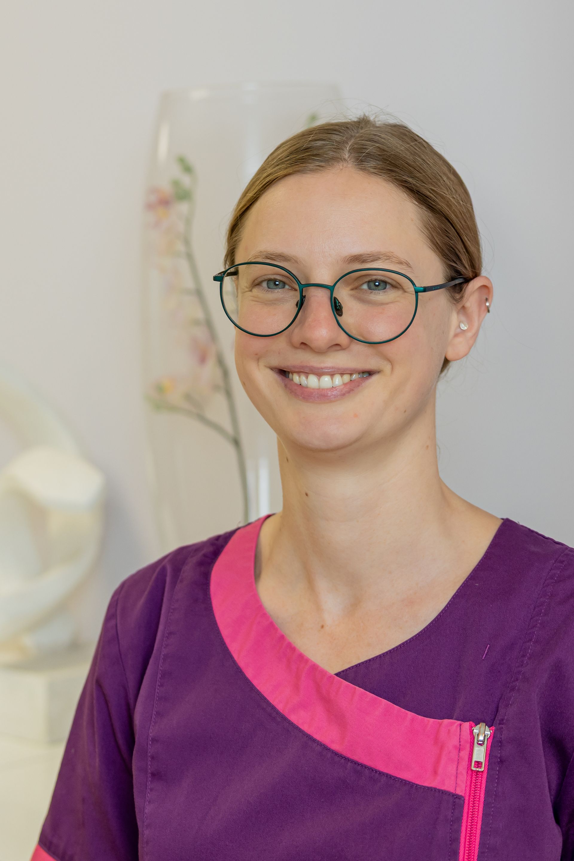 Frau mit langen, leuchtend roten Haaren lächelt in einem rosa Hemd in einem Büro.