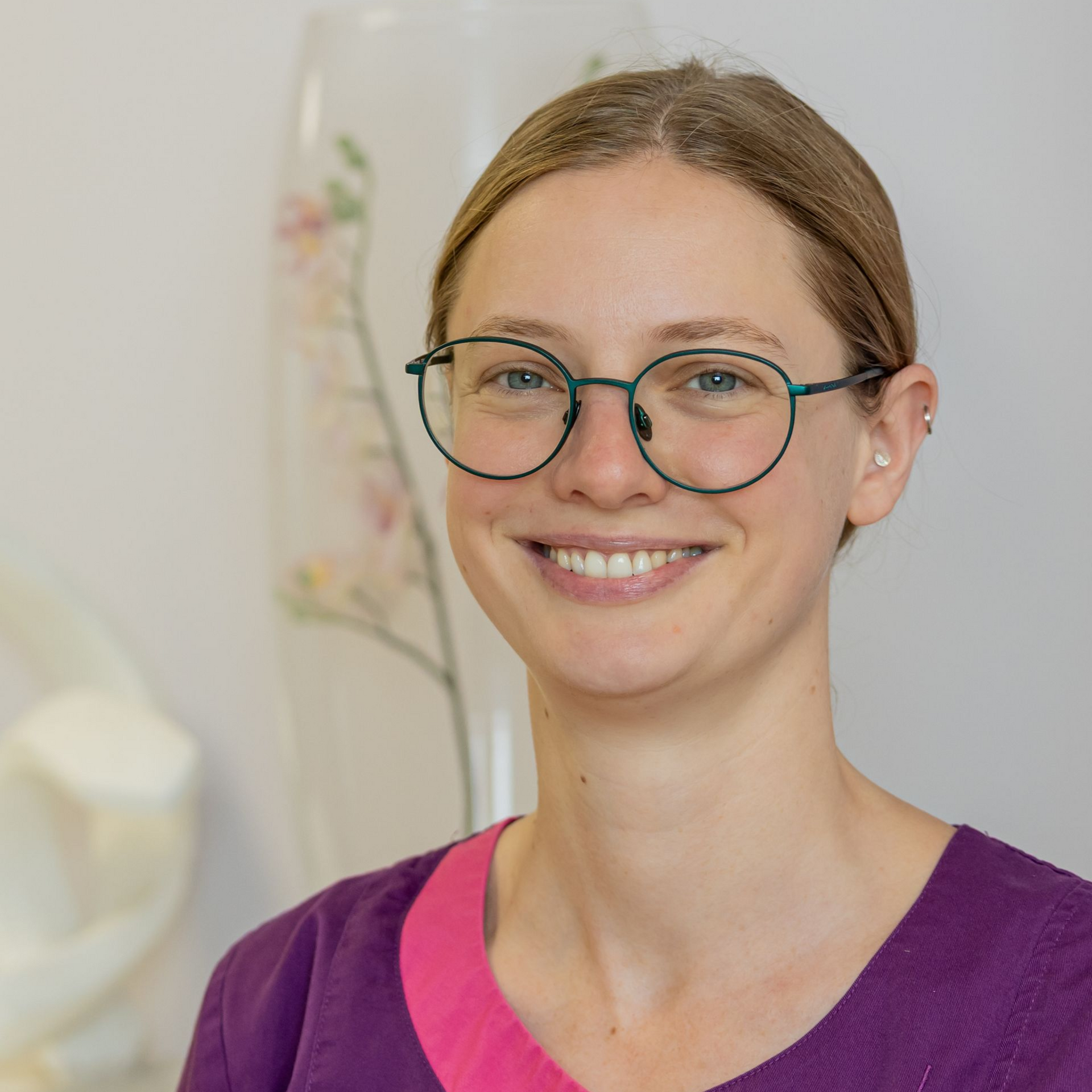 Frau mit langen, leuchtend roten Haaren lächelt in einem rosa Hemd in einem Büro.