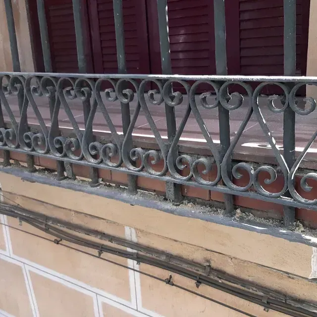 Un balcón con barandilla de hierro forjado y contraventanas.