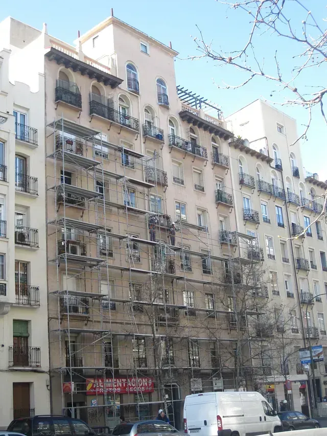 Una camioneta blanca está estacionada frente a un edificio con andamios.