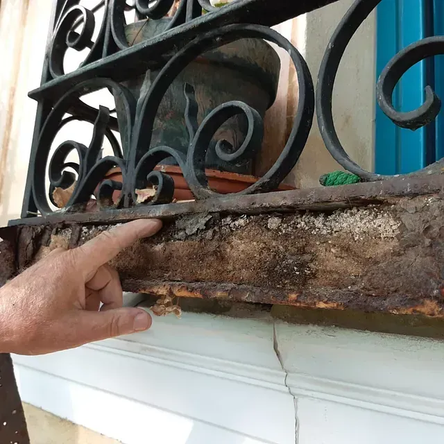 Una persona señalando una barandilla de hierro forjado en el alféizar de una ventana.