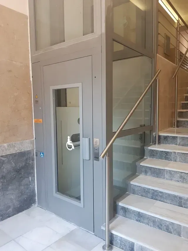 Un ascensor con un cartel para discapacitados en la puerta está al lado de un conjunto de escaleras.