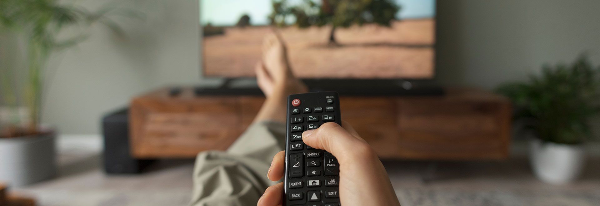 Télécommande de télévision tenue dans la main d'une personne assise dans un canapé