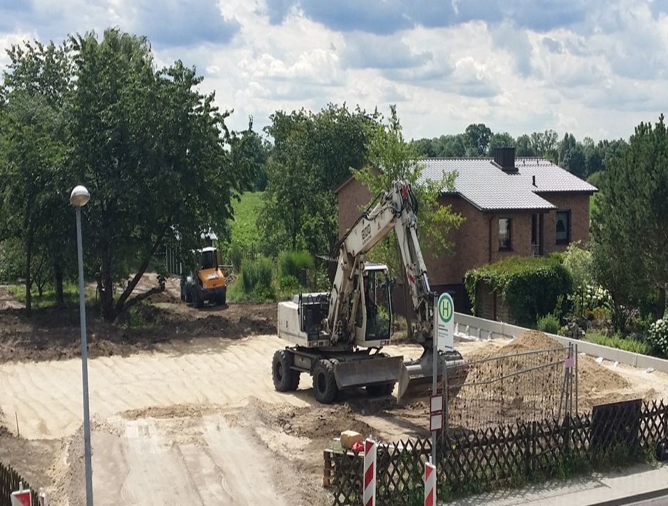Erdarbeiten mit Bagger auf großem baugrund mit haus im hintergrund