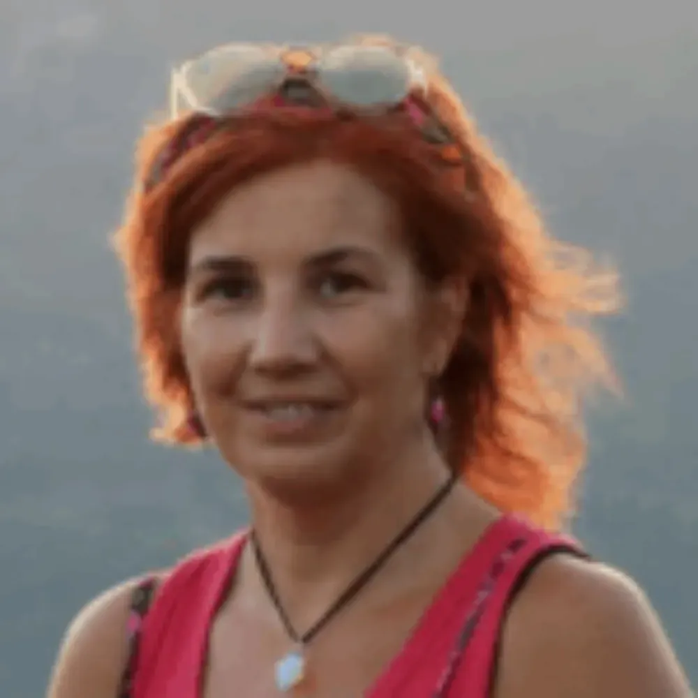 Una persona con cabello rojizo hasta los hombros, que lleva gafas de sol en la cabeza y una blusa rosa