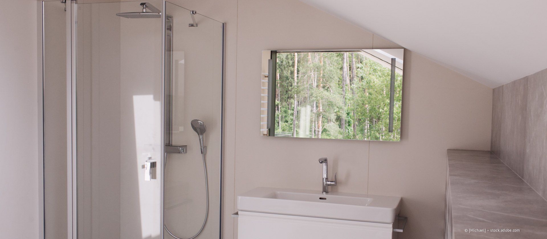 Badezimmer mit Dusche, Waschbecken, Spiegel und Dachschräge. Aus dem Fenster blickt man auf die Bäume draußen.