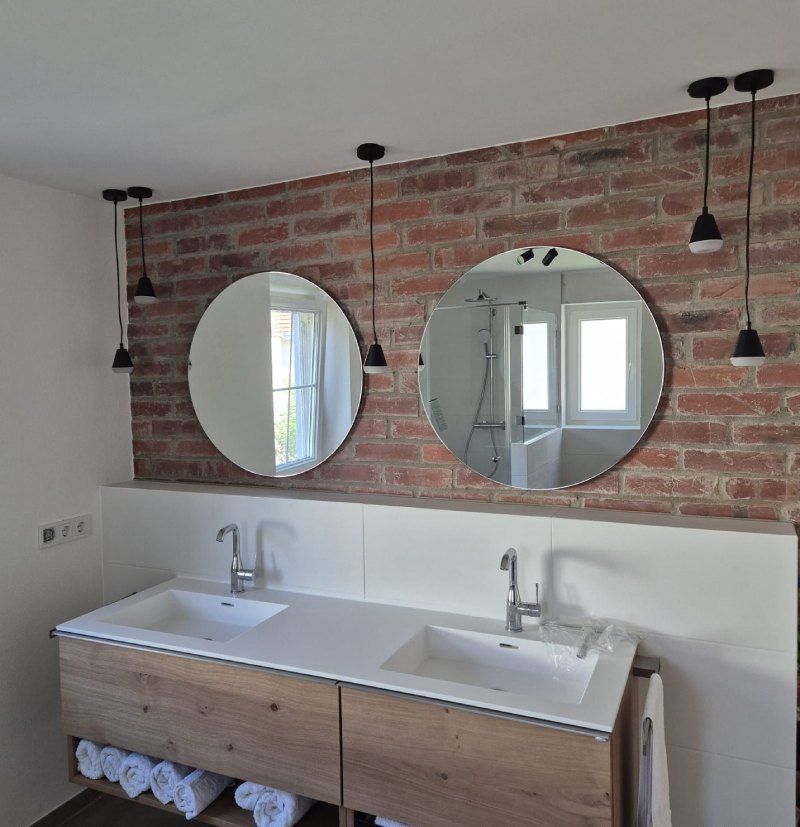 Badezimmer mit Backsteinwand, runden Spiegeln, Pendelleuchten und Waschtisch aus Holz mit Waschbecken.